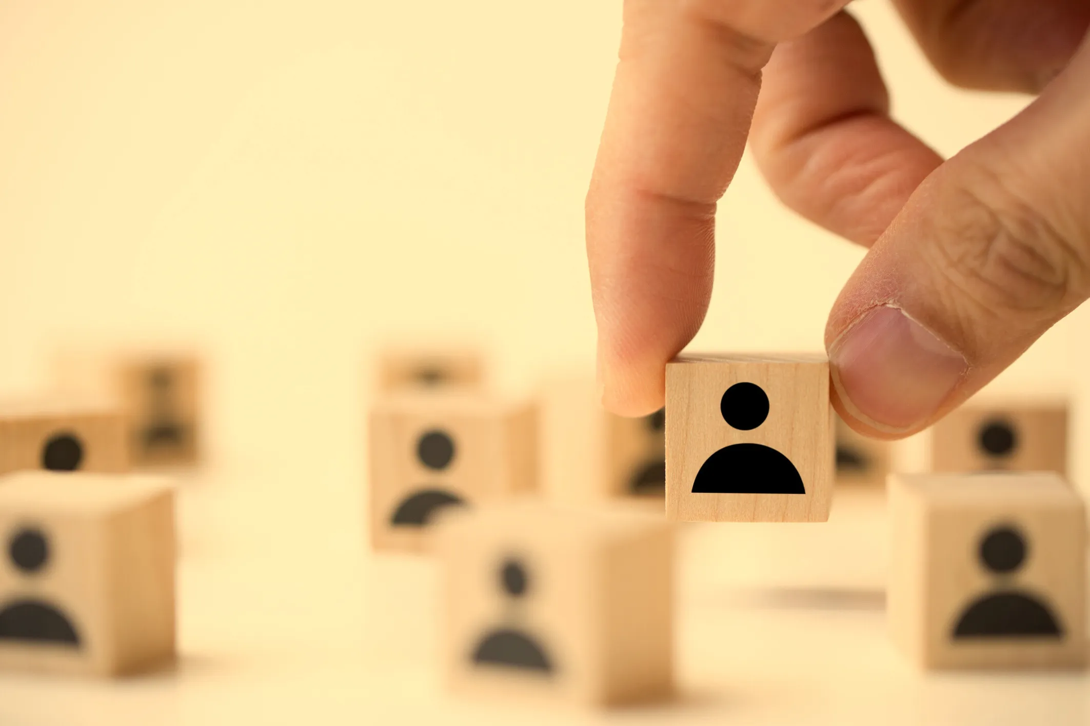 Hand picking up a wooden block with a person icon among other similar blocks symbolizing recruiting