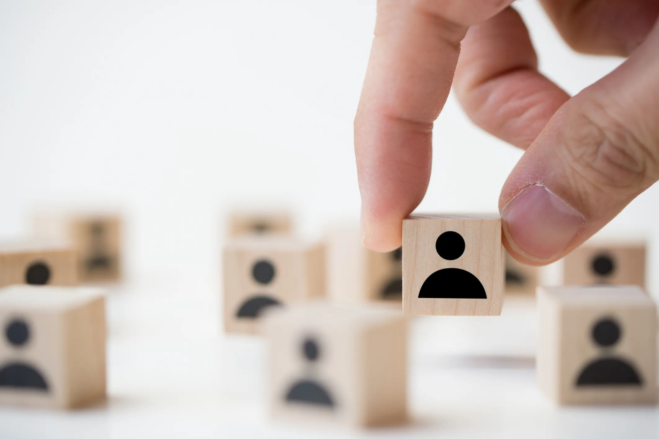 Hand picking up a wooden block with a person icon among other similar blocks symbolizing recruiting